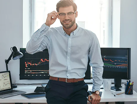 Confident financial advisor in corporate attire adjusting glasses in front of trading monitors.